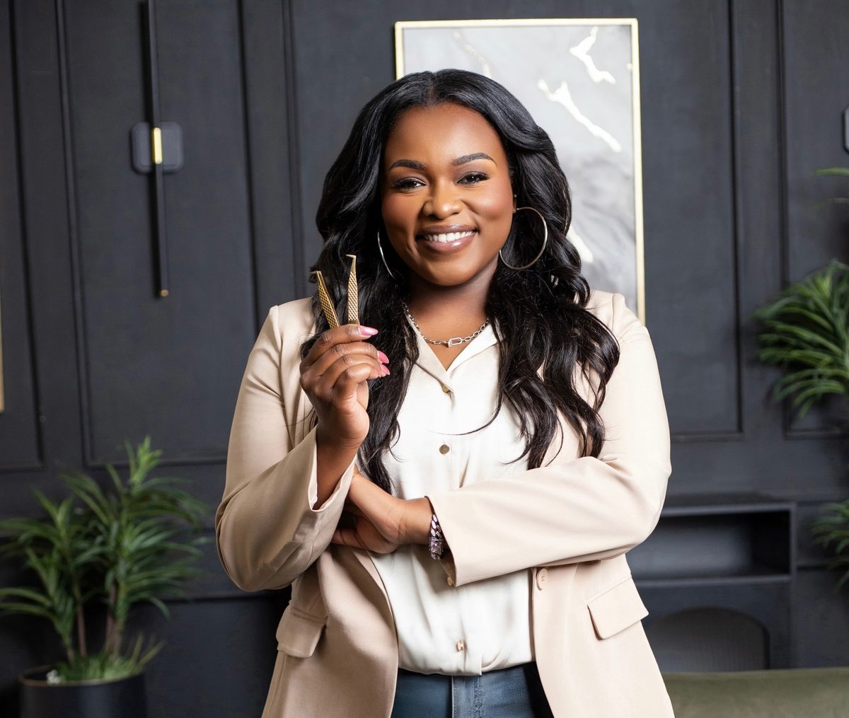 Tee, owner and lash artist at Minks & Pearls Studio, smiling and holding lash tweezers